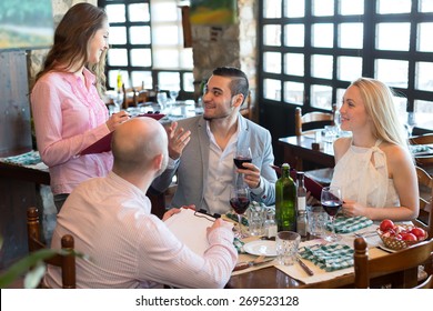 Cheerful waitress taking the order from visitors sitting at the table in a restaurant