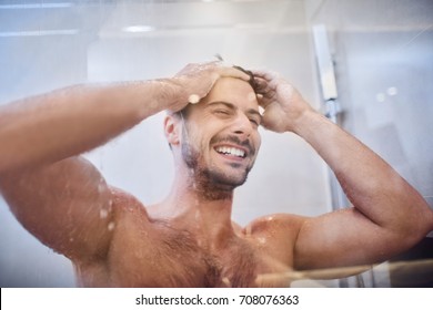 Cheerful well-built handsome young man laughing while in the shower 