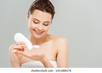 cheerful woman applying body lotion while holding bottle isolated on grey 