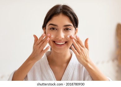 Cheerful Woman Applying Cream On Face Moisturizing Skin Smiling To Camera Posing In Bathroom Indoor. Facial Skincare Cosmetics, Female Beauty Routine Concept - Powered by Shutterstock