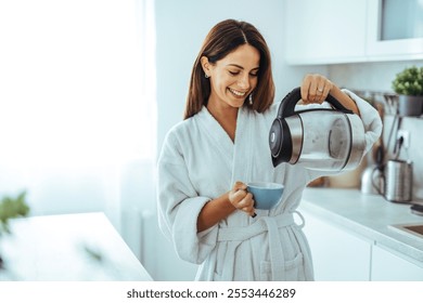 A cheerful woman in a bathrobe pours coffee in a bright, modern kitchen. The scene captures a relaxed morning routine with natural lighting and a sense of serenity. - Powered by Shutterstock