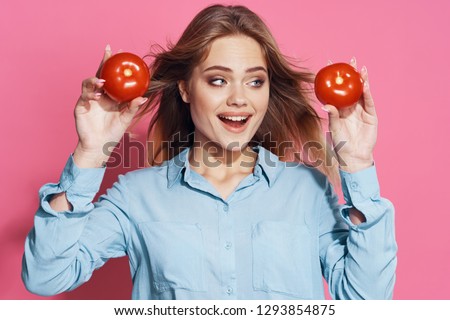 Cheerful woman in a blue shirt holds tomatoes in her hands on a pink background