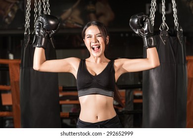 Cheerful Woman In Boxing Gloves Celebrating Victory. Happy Young Sporty Woman In Boxing Gloves Keeping Arms Raised While Standing At Gym