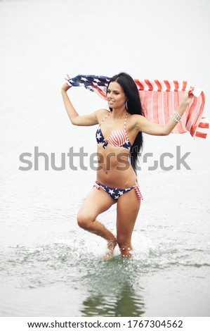 Cheerful woman celebrating US Independence Day on the beach with American flag