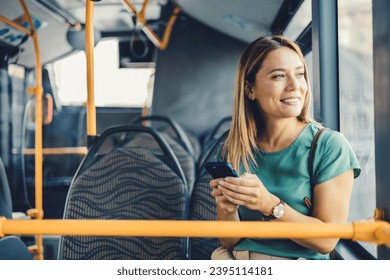 Cheerful woman with cell phone in public transportation. Smiling young woman with cell phone in public transportation. Woman uses mobile app while riding commuter train