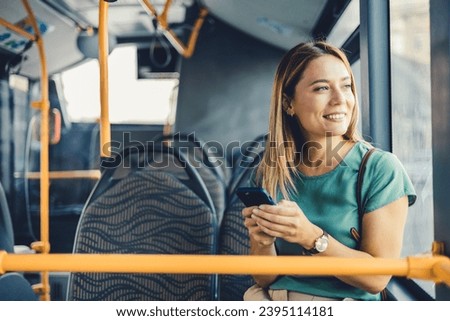 Cheerful woman with cell phone in public transportation. Smiling young woman with cell phone in public transportation. Woman uses mobile app while riding commuter train