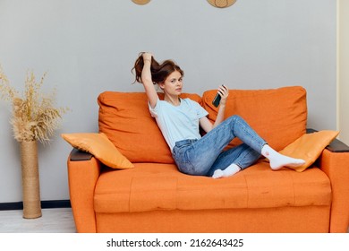 Cheerful Woman Chatting On The Orange Couch With A Smartphone Apartments