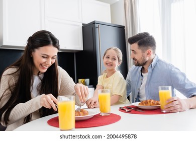 cheerful woman cutting croissant during breakfast with husband and daughter - Powered by Shutterstock