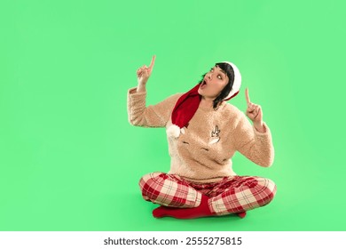 Cheerful woman in festive sweater and hat poses with playful gestures against vibrant green background - Powered by Shutterstock