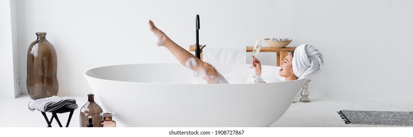 Cheerful woman with glass of champagne bathing at home, banner