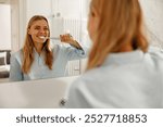 A cheerful woman happily enjoys her morning routine while brushing her teeth in a bright, sunny bathroom