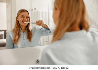 A cheerful woman happily enjoys her morning routine while brushing her teeth in a bright, sunny bathroom - Powered by Shutterstock