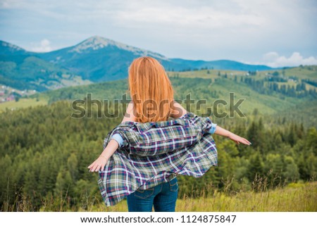 Cheerful woman is having rest on the edge of the cliff and looking at the valley and mountains. Traveling along the mountains, freedom and active lifestyle concept