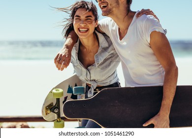 Cheerful woman with her boyfriend walking by the beach. Couple with skateboards having fun at the beach. - Powered by Shutterstock