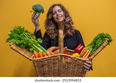 A cheerful woman holding a picnic basket brimming with fresh fruits and vegetables, radiating health and wellness. The vibrant yellow background enhances the lively, joyful atmosphere of the scene - Powered by Shutterstock