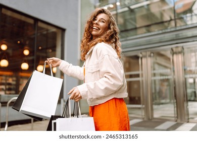 Cheerful woman holding shopping bags. Beautiful woman in casual style shopping in the city. Consumerism, purchases, shopping, lifestyle, sale concept - Powered by Shutterstock