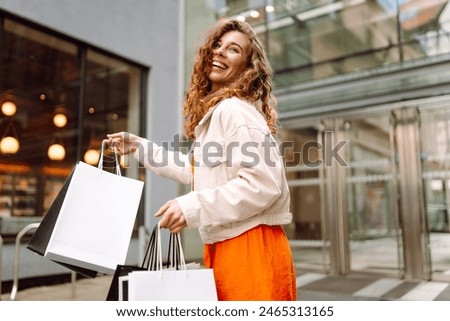 Cheerful woman holding shopping bags. Beautiful woman in casual style shopping in the city. Consumerism, purchases, shopping, lifestyle, sale concept