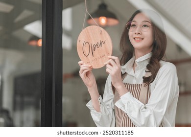 A cheerful woman holds an "Open" sign in a café, ready to welcome customers with a friendly smile. - Powered by Shutterstock