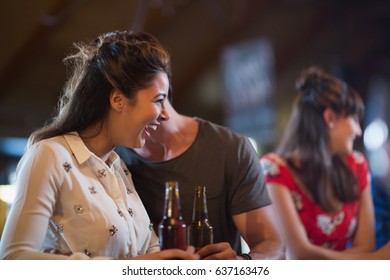 Cheerful woman looking away while holding beer bottle in bar