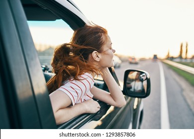 A Cheerful Woman Looks Out Of The Window Of The Car Going Down The Road