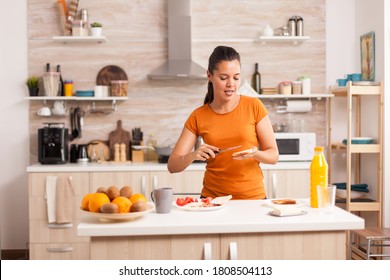 Cheerful woman in the morning singing and spreading butter on roasted bread. Knife smearing soft butter on slice of bread. Healthy lifestyle, making morning delicious meal in cozy kitchen. Traditional
