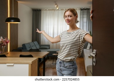 Cheerful woman opening house front door and inviting friends. Young woman welcoming visitors in her home.	 - Shutterstock ID 2257024855