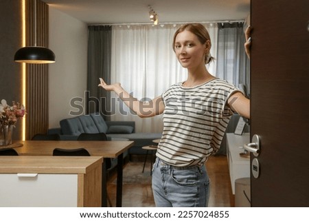 Cheerful woman opening house front door and inviting friends. Young woman welcoming visitors in her home.	