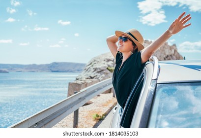 Cheerful Woman portrait enjoying the seaside road trip. Dressed a black dress, straw hat and sungllasses she wide opened arms and shining with happiness. Summer vacation traveling by auto concept. - Powered by Shutterstock