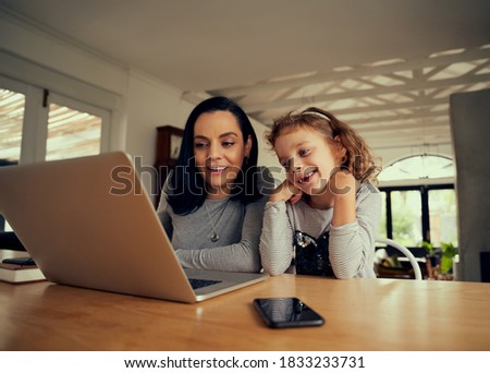 Cheerful woman with preschool daughter watching funny videos on laptop at home