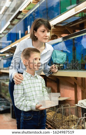 Cheerful woman with preteen son looking for aquarium fishes for in pet store

