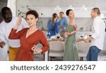 Cheerful woman in reddish brown dress enjoying active dancing with friends of different nationalities at casual relaxed home gathering..