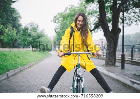 Cheerful woman riding bicycle and wearing yellow raincoat. Young woman cycling in the raincoat

