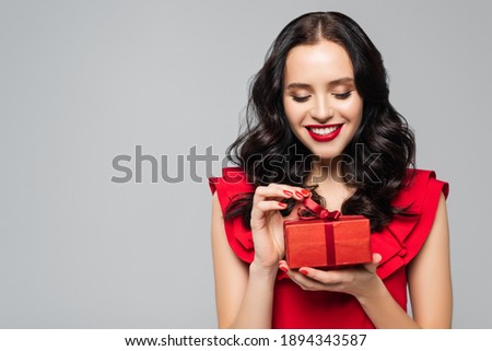 cheerful woman in ruffled dress pulling ribbon on gift box isolated on grey