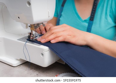 Cheerful woman sewing while sitting at her working place in fashion workshop
