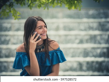 Cheerful woman sitting and talking phone. Horizontal outdoors shot.