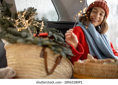 A Cheerful Woman Smiling And Looking At Sparkler While Sitting In Car Trunk , Traveling By Car During Christmas Holidays. High Quality Photo