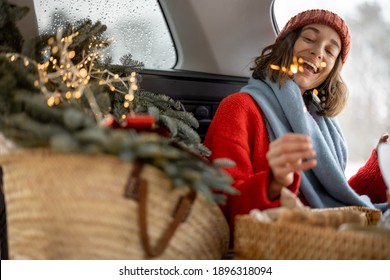 A Cheerful Woman Smiling And Looking At Sparkler While Sitting In Car Trunk , Traveling By Car During Christmas Holidays. High Quality Photo