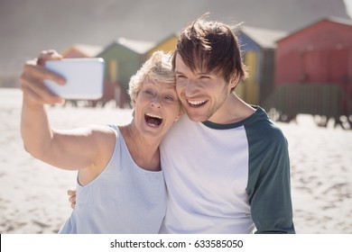 Cheerful woman with son taking selfie at beach during sunny day - Powered by Shutterstock