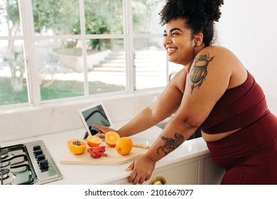 Cheerful Woman Standing At Kitchen With Fruits And Tablet Pc. Body Positive Female In Exercise Outfit Working At Kitchen.