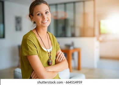 Cheerful woman standing in living-room with arms crossed - Shutterstock ID 664514959