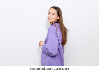 a cheerful woman stands on a white background on the floor sideways in a purple tracksuit slightly hunched over holding a canopy with her hands joined together smiling happily turning her head forward