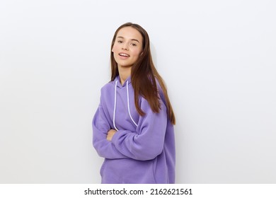 a cheerful woman stands sideways on a white background in a purple tracksuit, slightly hunched over, lowered her arms crossed together, smiling happily