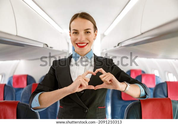 Cheerful\
woman stewardess doing heart sign in\
airplane