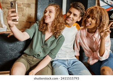 cheerful woman taking selfie with multiethnic friends while having fun in lobby of youth hostel