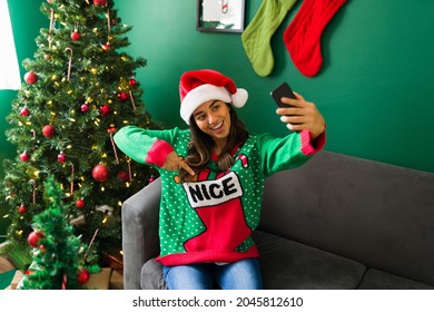 Cheerful Woman Taking A Selfie With A Smartphone And Showing Her Ugly Christmas Sweater On Social Media