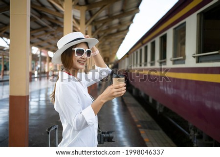 Cheerful woman traveler waiting for train on railway station.
