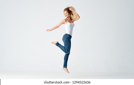 Cheerful woman in a t-shirt and jeans barefoot bounces up on a gray background
