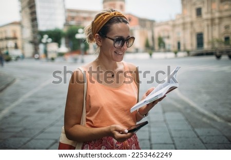 Cheerful woman wander with travel guidebook and smart phone