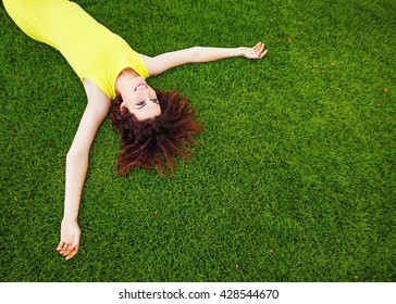 Cheerful Woman Wearing Bright Dress Lying Down On A Grass