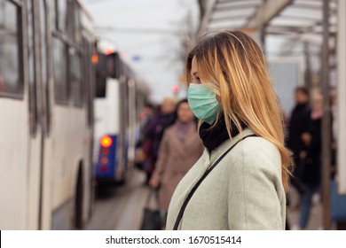 Fröhliche Frau mit einer sterilen medizinischen Schutzmaske gegen Coronavirus, Covid-2019 Asiatisches Pandemie-Särvirus an öffentlichen Busbahnhöfen in der europäischen Stadtstraße, Menschen auf dem Hintergrund